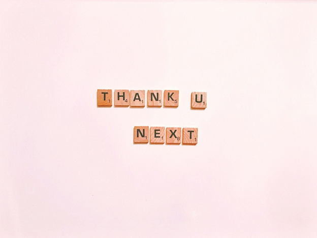 Scrabble tiles spell "THANK U, NEXT" on a soft pink background.