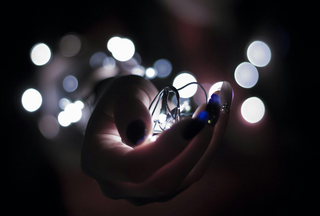 A hand gently holds glowing string lights in a dark setting.