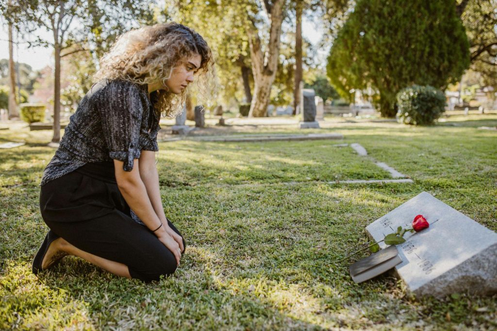 A woman kneels by a gravestone, reflecting on the signs from loved ones after death.