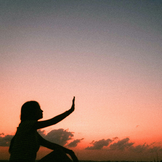 Silhouette of a person with raised hand against a dramatic sunset sky.