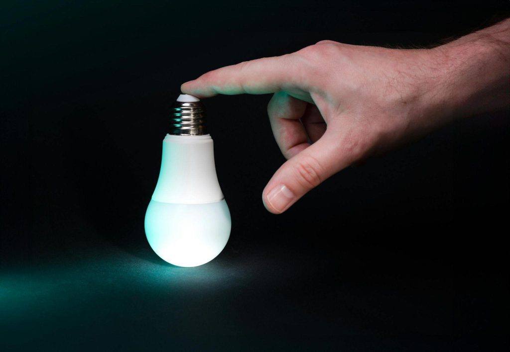 A hand touches the top of a glowing light bulb, conveying how to trust intuition without fear.