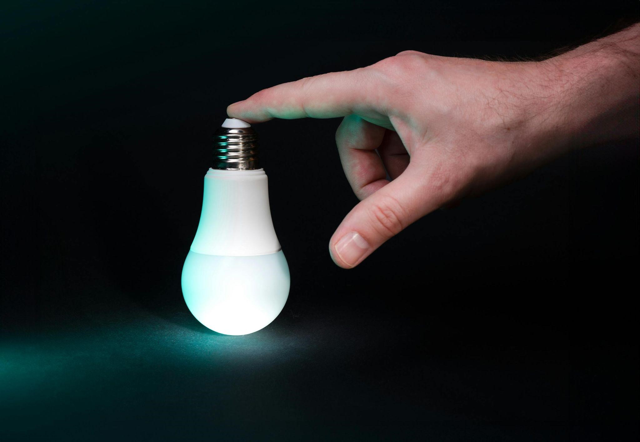 A hand touches the top of a glowing light bulb, conveying how to trust intuition without fear.