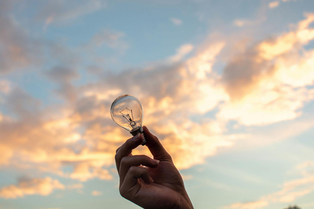 A hand holds a light bulb against a sunset soft sky, embracing intuition.